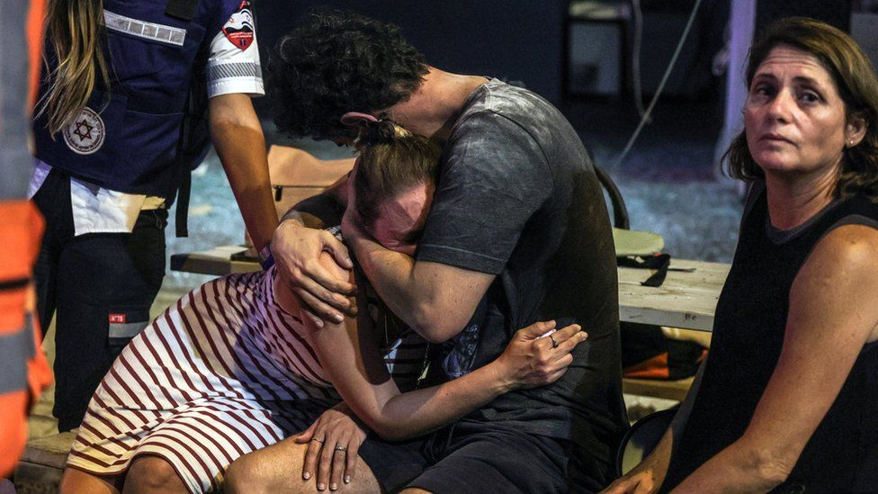 People react at the site where a rocket launched from the Gaza Strip landed in Tel Aviv, Israel