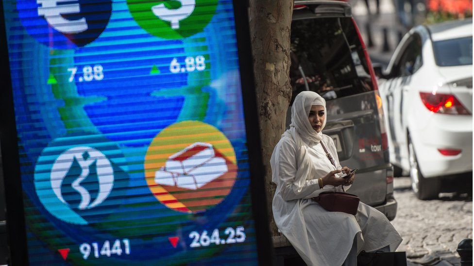 A woman sits beside a digital billboard giving market updates in Istanbul in August 2018