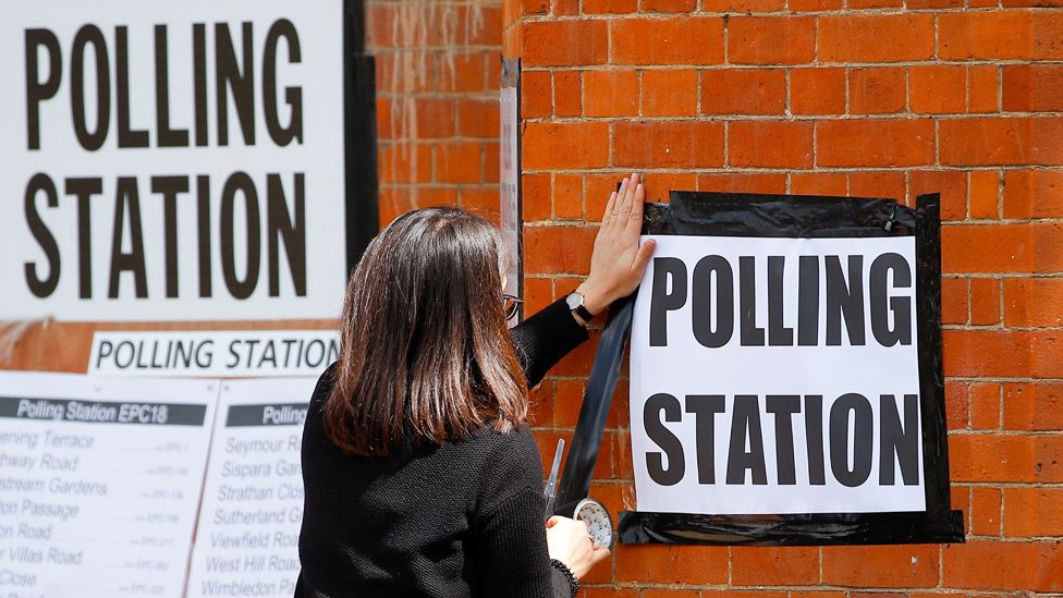 A woman attaches a sign on the wall of a polling station