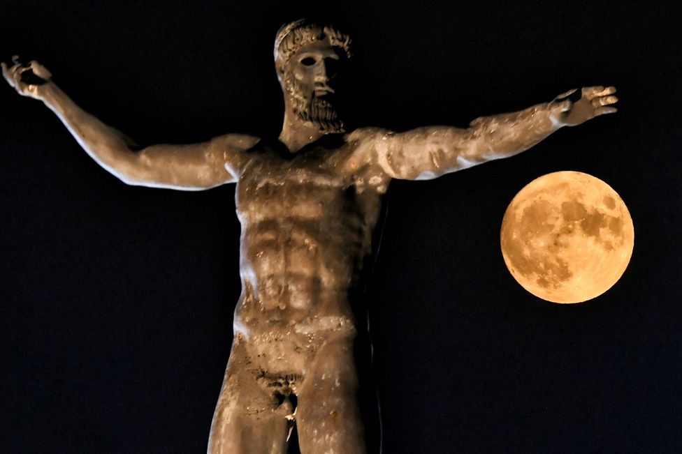 The moon rises above the statue of the Ancient Greek god Poseidon in Ancient Corinth near Athens, Greece
