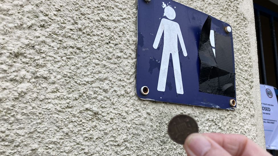 A coin being held outside a public toilet