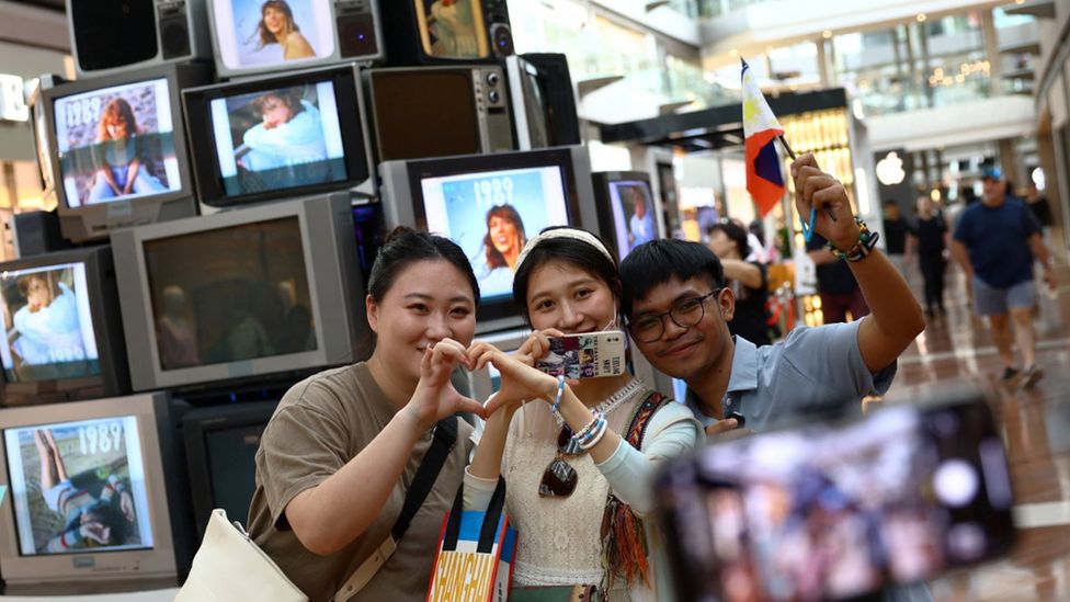 Fans, one holding a Philippines flag, pose for a picture in front of a Taylor Swift installation in Marina Bay Sands shopping mall in Singapore