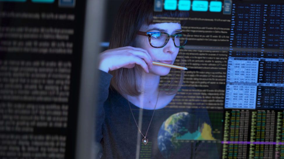 Una mujer mira a través de pantalla de computadora transparente