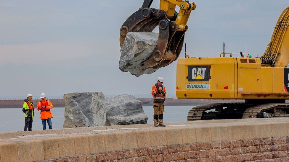 Boulder being moved by arm of crane