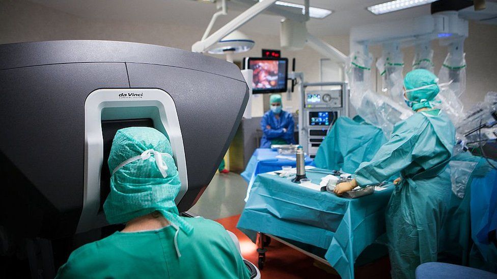 A surgeon (left) uses a da Vinci surgical robot, controlled by a console, to perform a hysterectomy