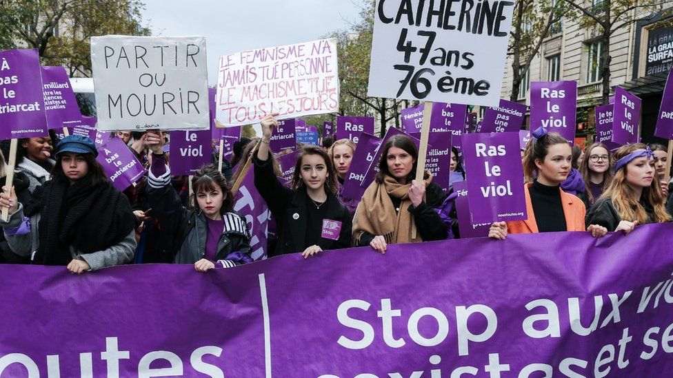 Women carry purple protest signs