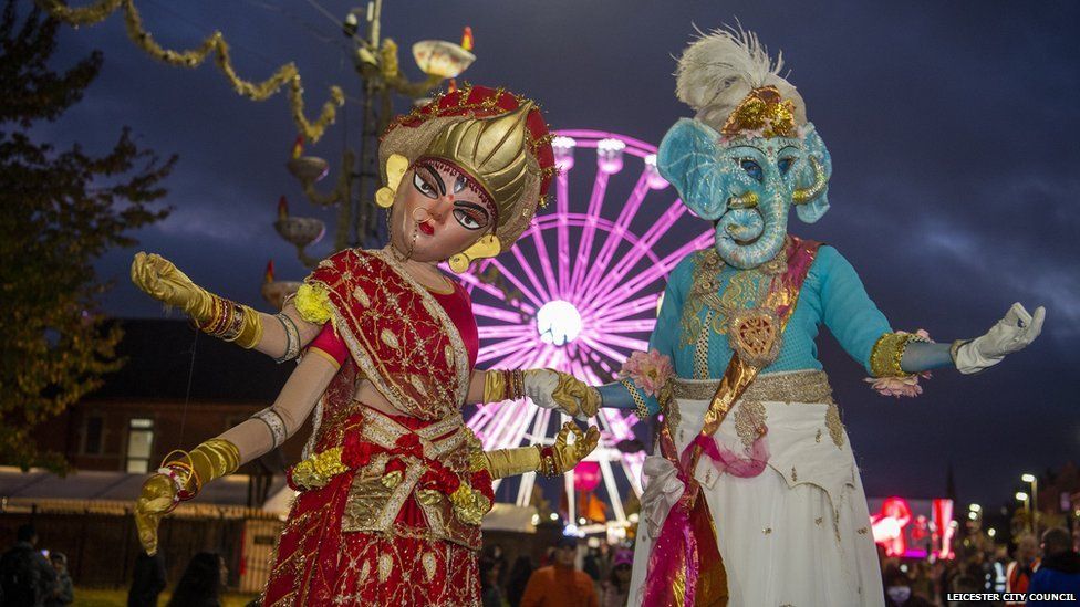 People dressed up as hindu gods with wheel of lights in background