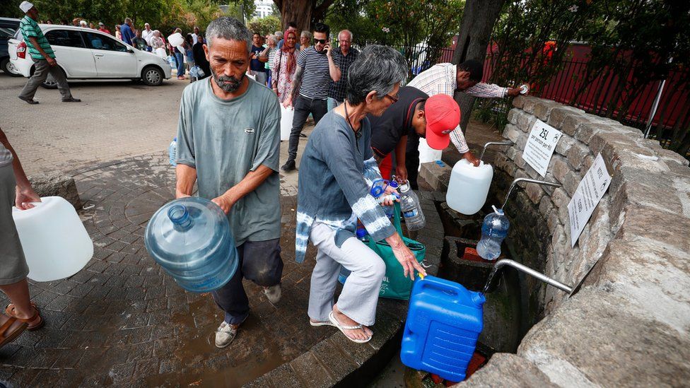 Cape Town residents filling up water tanks at a mountain spring point, with a long queue behind