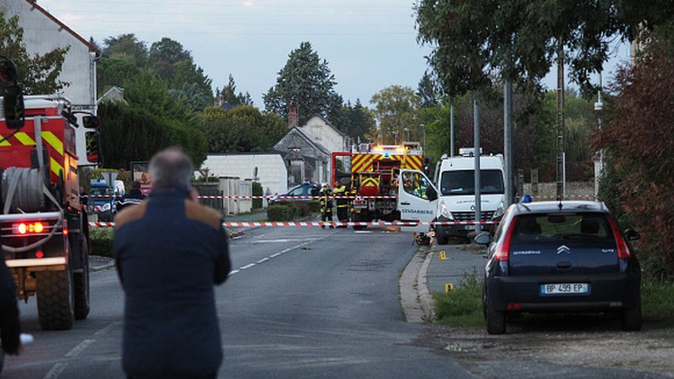 A man stands as French gendarmes and firemen work next to the site where an ULM crashed in Loches
