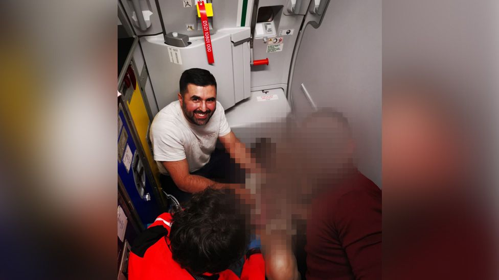 Hassan Khan poses with the baby and her mother, whose faces have been blurred, on the plane