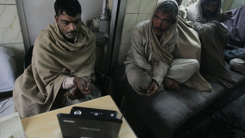 Two Indian labourers follow news on a laptop computer