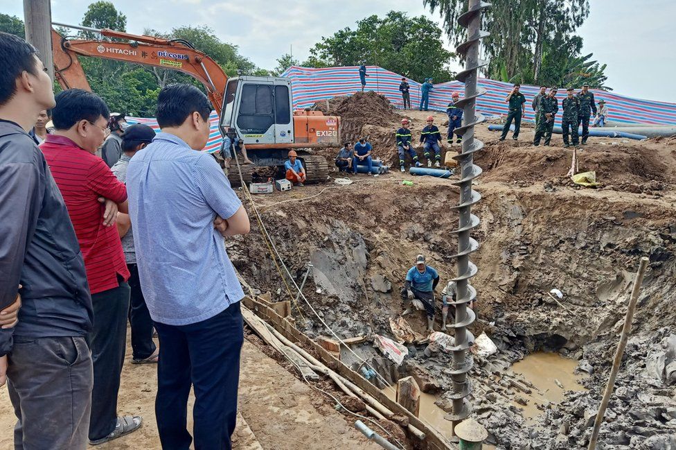 Rescuers look down into the site of where a 10-year-old boy is thought to be trapped in a 35-metre deep shaft at a bridge construction area in Vietnam's Dong Thap province on January 2, 2023