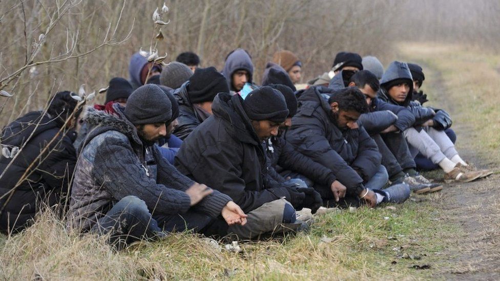 Detained migrants who arrived via Serbia sit near the border village of Roszke, Hungary, 9 February 2016