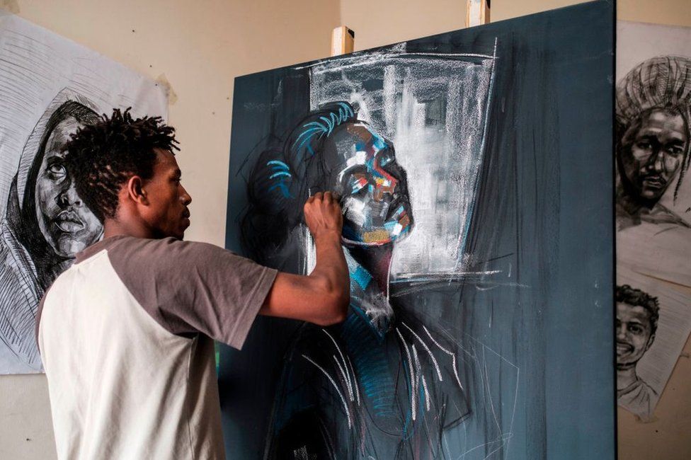 A man uses coloured paint and chalk on a dark canvas.