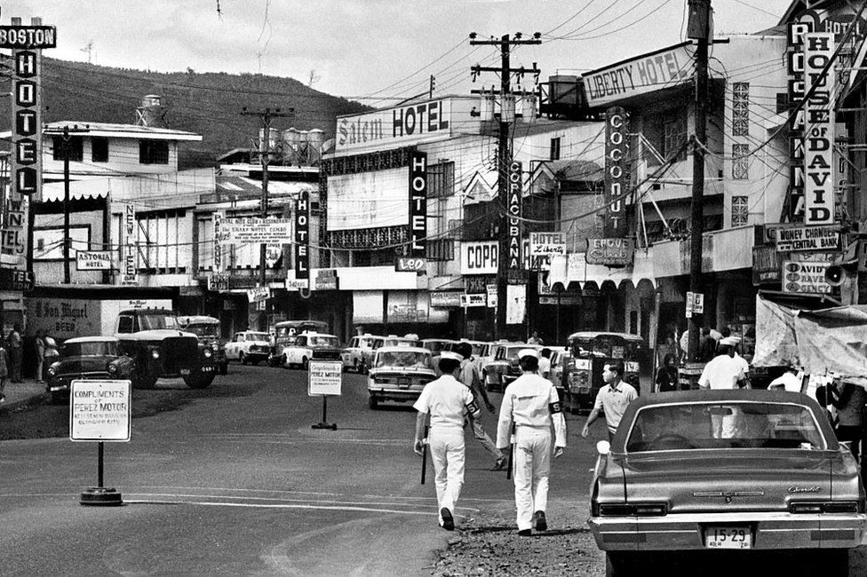 A pair of U.S. Navy shore patrol officers walk through Olongapo, a city in the Philippines often referred to as Olongapo City. Olongapo was a popular destination for U.S. Navy sailors stationed at the adjacent U.S. Naval Base Subic Bay.