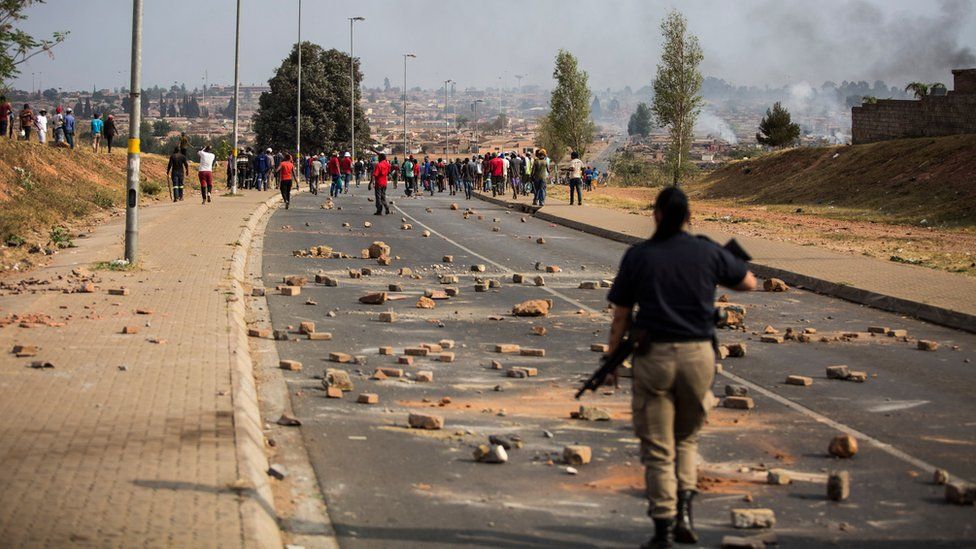 Сотрудник столичной полиции наблюдает за толпой бунтовщиков в Йоханнесбурге в начале этого месяца