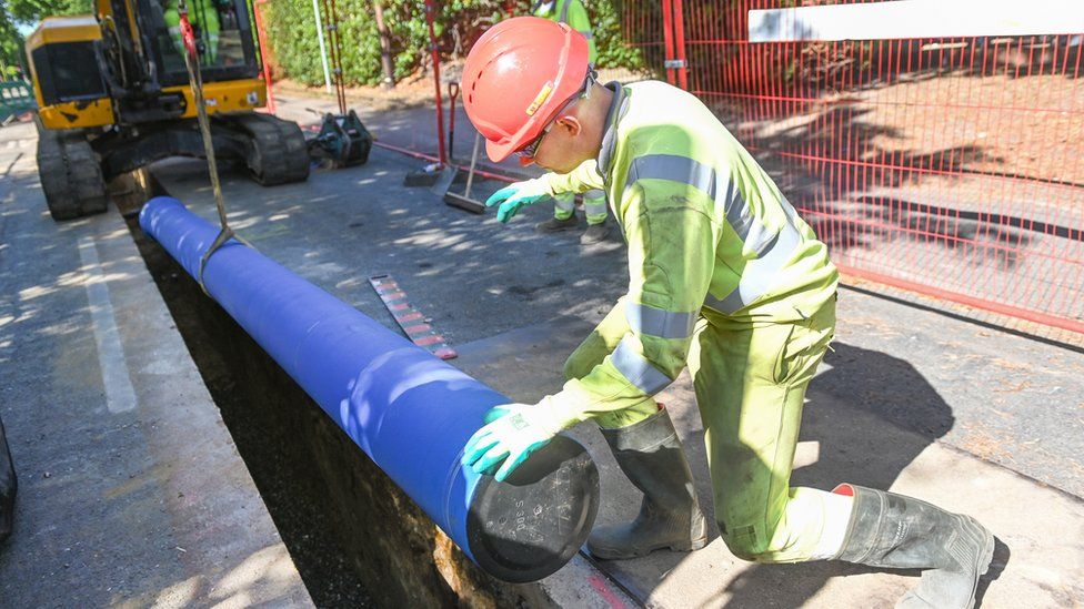 A worker in hi-vis and a helmet laying a new pipe in the road