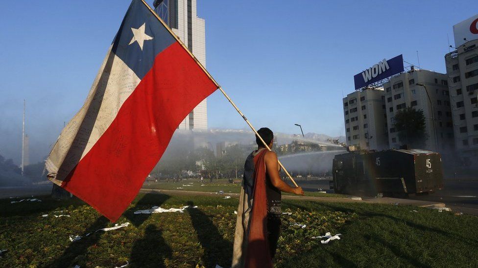 A man holds a Chilean flag in front of a tank