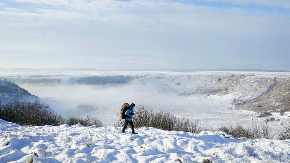A person walks through snow above the Hole of Horcum at the North York Moors National Park, as scattered weather warnings for snow and ice are in place across the UK as temperatures plunged below freezing overnight.