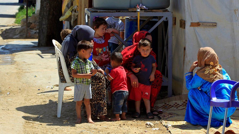 Syrian refugees sit with their children outside tents at a camp in the eastern Lebanese town of Saadnayel (19 July 2016)