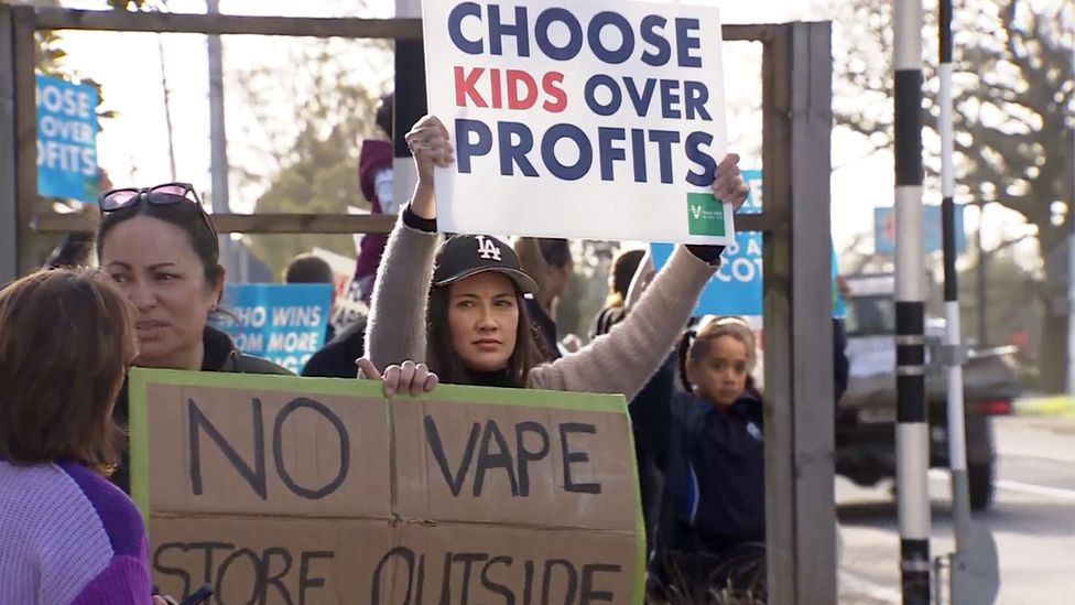 Parents in Auckland stand holding billboards in protest against vaping shops opening near to schools