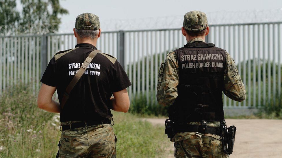 Polish border guards face a tall metal fence at the border with Belarus