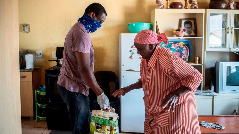 A volunteer from the Rays of Light NGO (L) delivers food and cleaning products to an elderly woman (R) living alone in Alexandra, Johannesburg, on April 16, 2020.