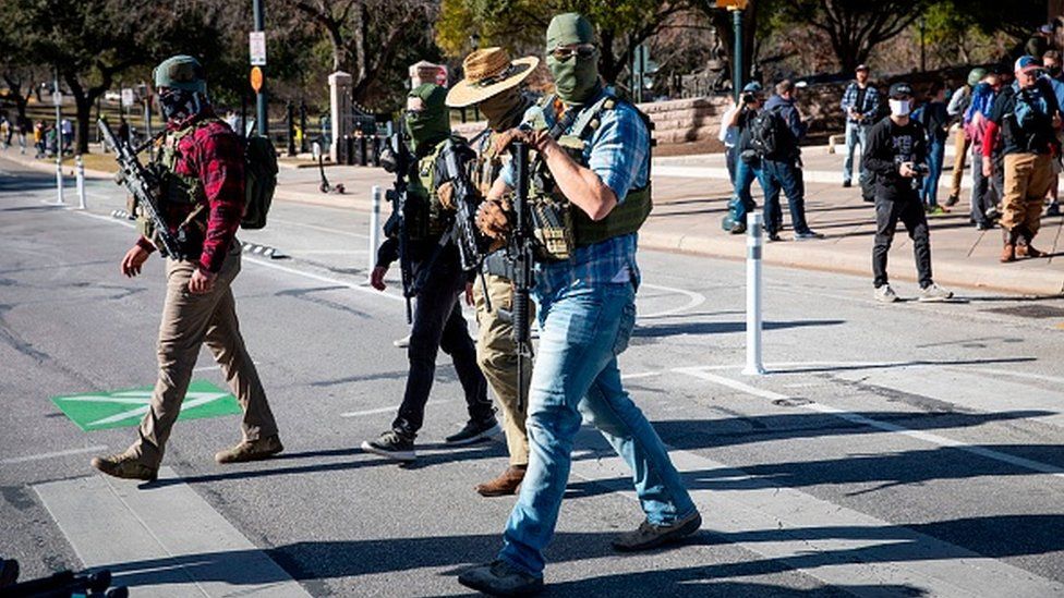 Armed groups cross the street as they hold a rally in front of a closed Texas State Capitol in Austin, Texas
