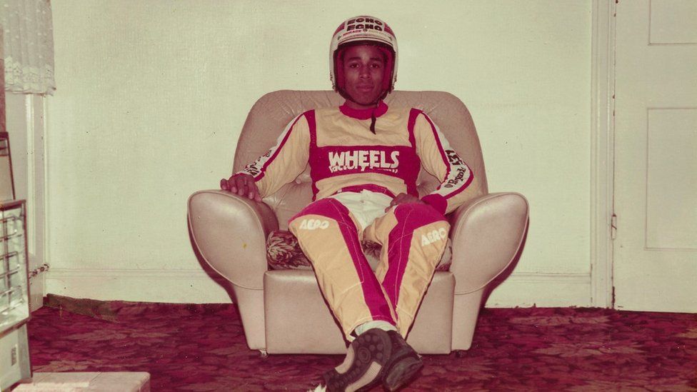 Young man in helment and cycling gear sitting on an armchair in a living room