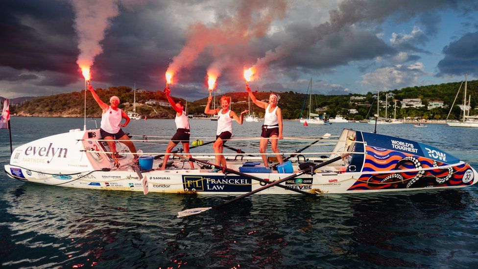 Four women on-board a rowing boat with flares