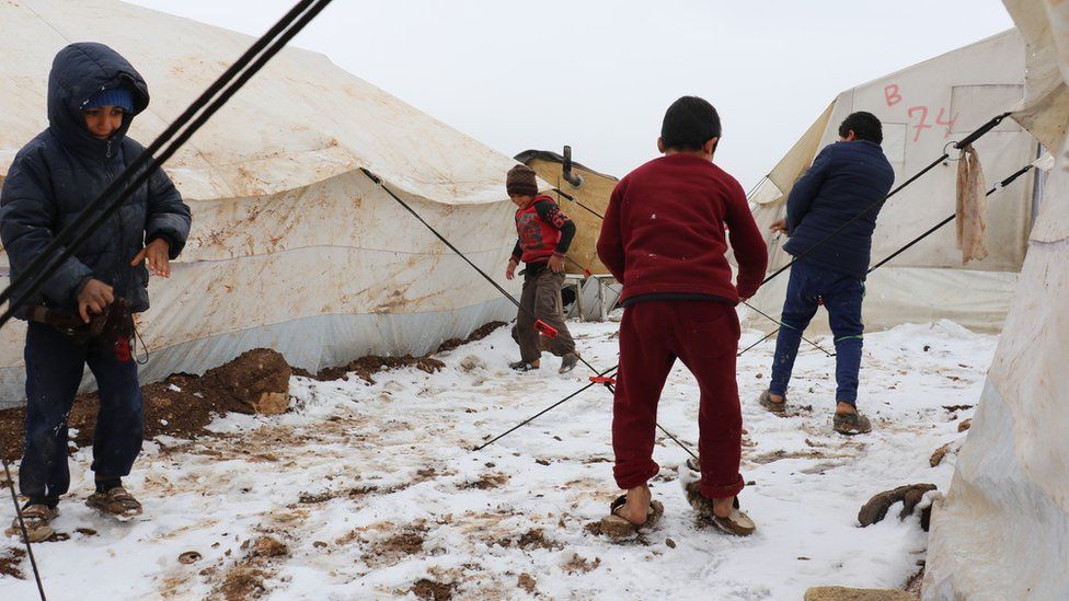 Children stand in the snow at a camp for displaced people in Aleppo province, Syria