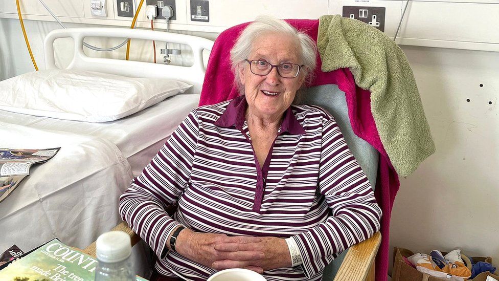 Gwendaline Bawden sentada junto a su cama de hospital