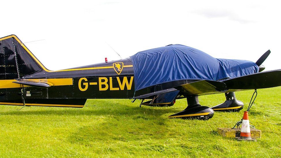 Black light plane with yellow trim and sheet over the cockpit