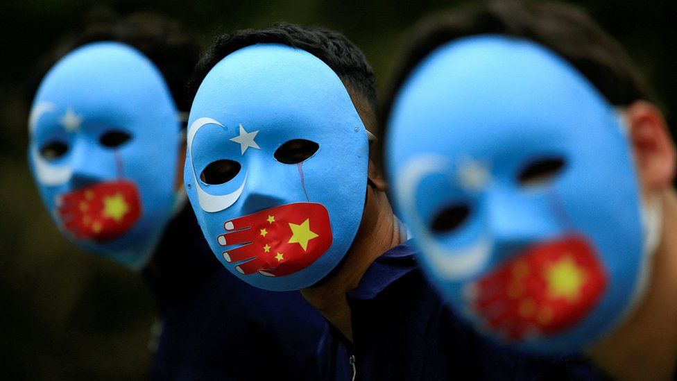 Three people wear blue masks with the Islamic star and crescent and the China flag covering their mouths