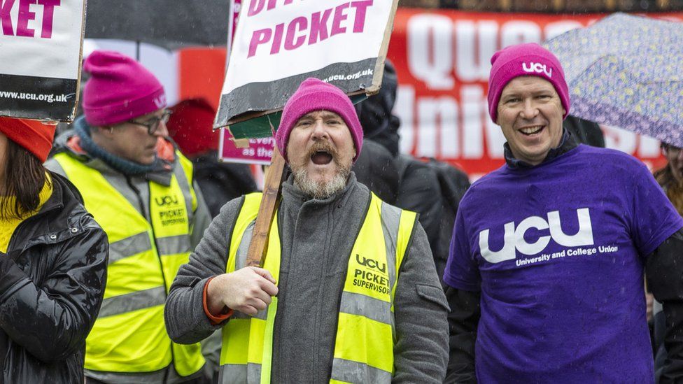 Striking Queen's University staff hold placards and chant on the picket line