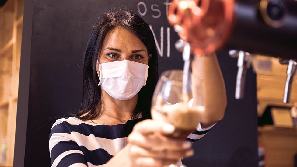 Barmaid with a mask pouring a drink