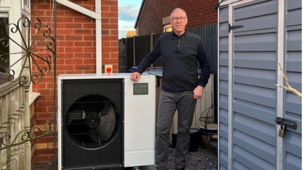 Anthony Hibbs stands next to his heat pump at the back of his house