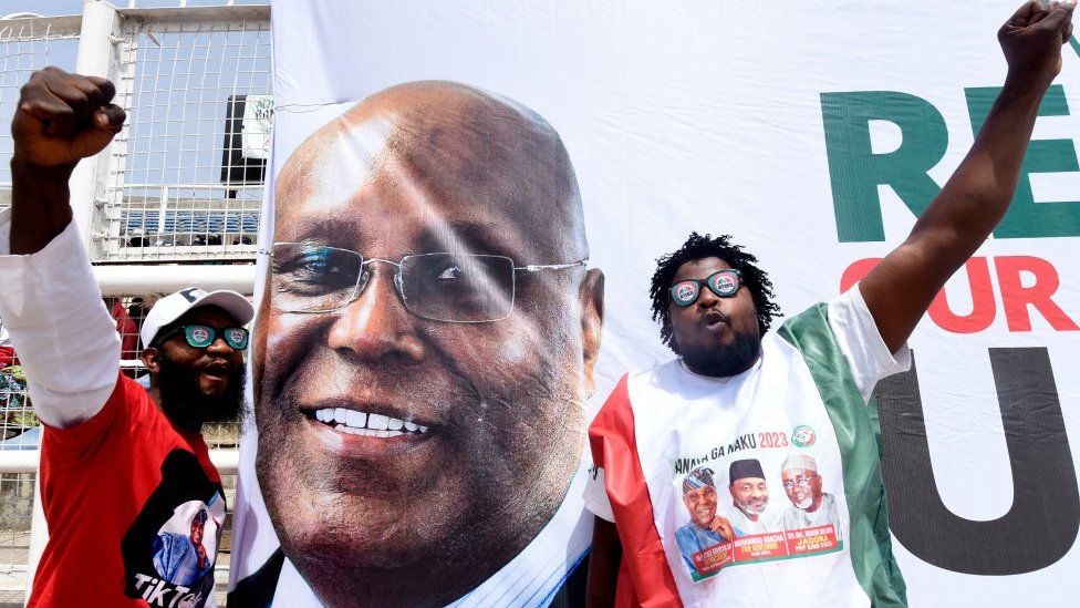 Supporters gesture next to the banner of the candidate of the opposition Peoples Democratic Party (PDP) Atiku Abubakar during a campaign rally in Kano, Nigeria - 9 February 2023