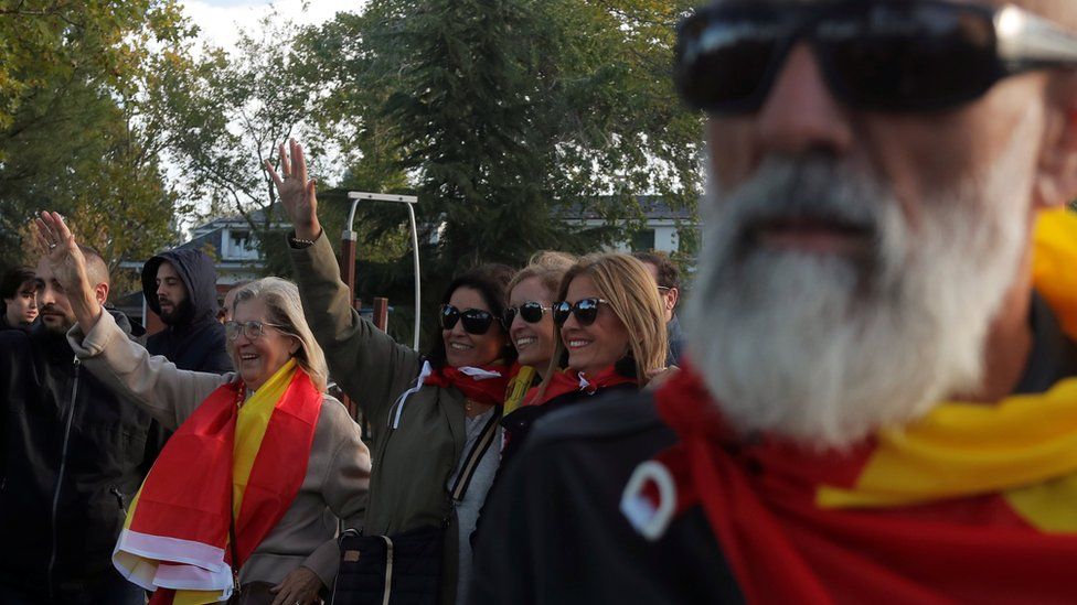 Franco supporters draped in Spanish flags wave outside the El Pardo cemetery where he will be re-buried