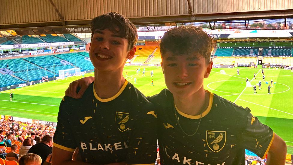 Jake, left, and Henry, right, standing in the crowd at Carrow Road, with the pitch in the rear showing a training session