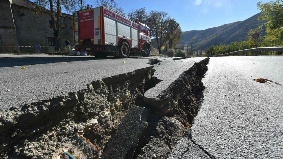 Fire engine passes near cracks on the road outside the center of Norcia