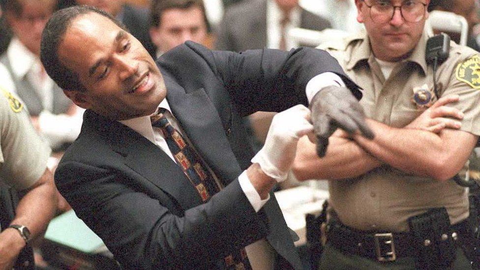 Double murder defendant O.J. Simpson puts on one of the bloody gloves as a Los Angeles Sheriff's Deputy looks on during the O.J. Simpson murder trial 15 June. One of the gloves was found at the murder scene, while the other was found at Simpson's state.