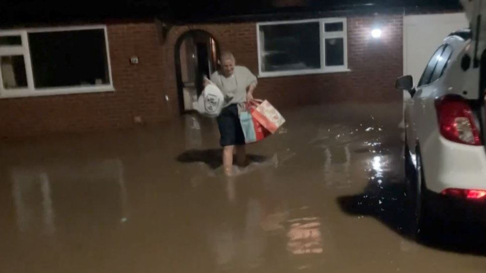 Woman carrying her belongings through flood water in Ruthin