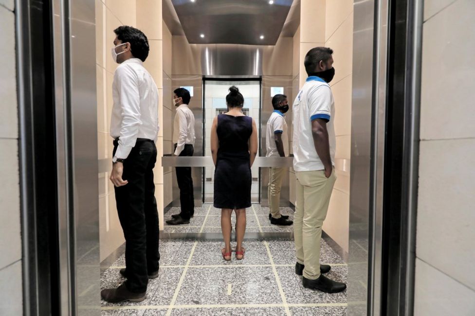 People face away from each other as they practise social distancing inside a lift