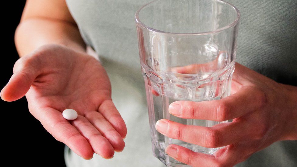 Woman holding a pill and a glass of water