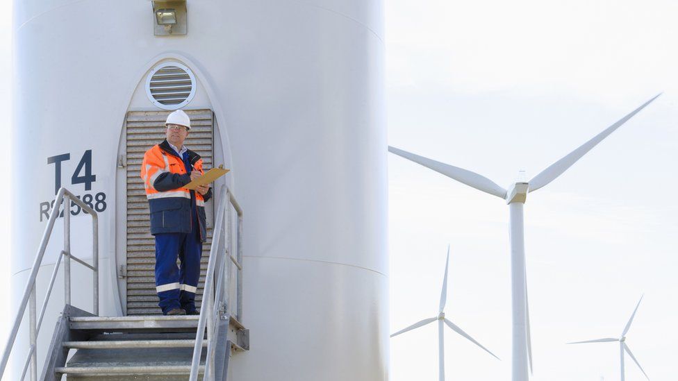 Technician reading paperwork near wind turbine