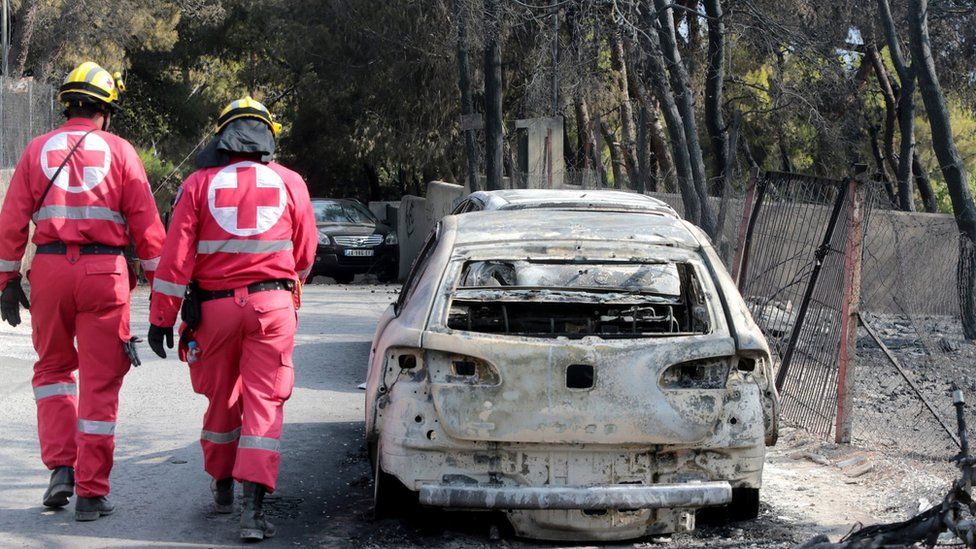 Members of the Red Cross search the area past burned cars after a fire in Mati, Greece, 24 July 2018