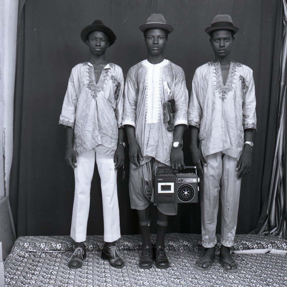 Three Malian men stand holding a boombox looking very serious