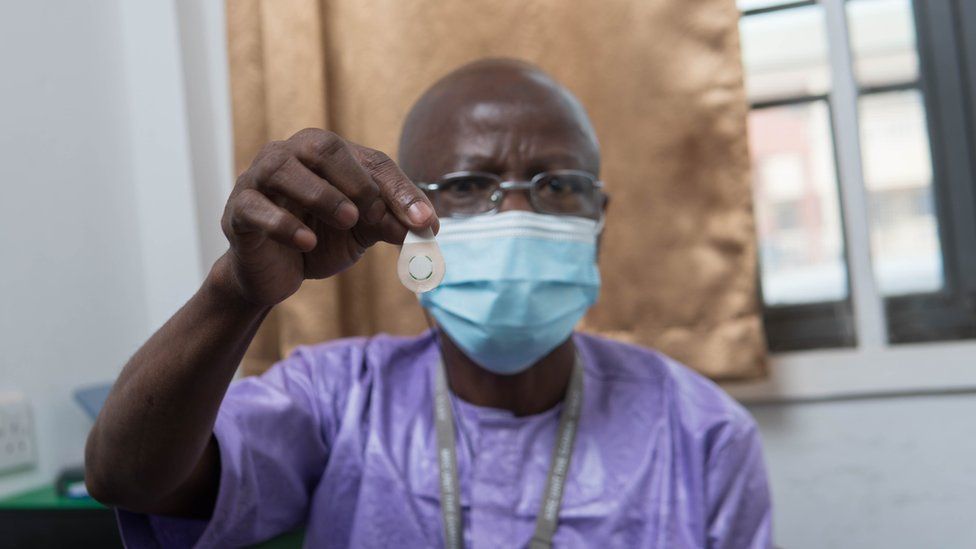 A healthcare worker in The Gambia holds up a microarray patch of the type used in the study.