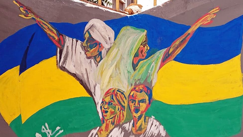 A man, woman and two children depicted on a mural in front of Sudan's old flag - Khartoum, Sudan